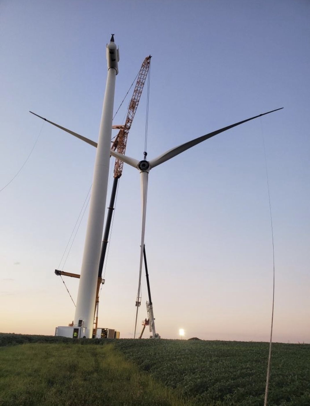 Wind turbine assembled with crawler crane behind it at sunset