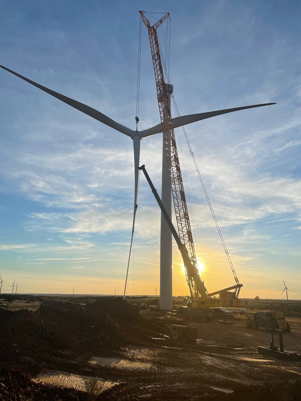 Crawler crane erecting wind turbine at sunset