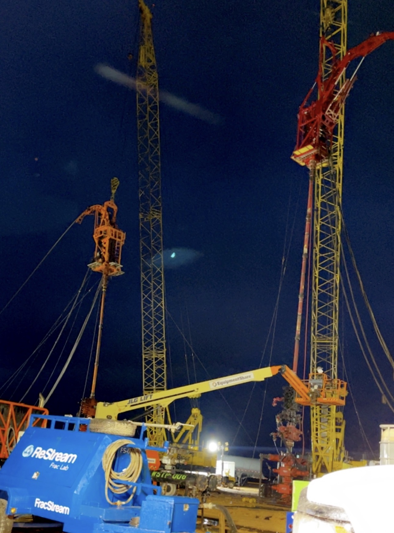 Two cranes supporting coiled tubing operations on a frac site at night